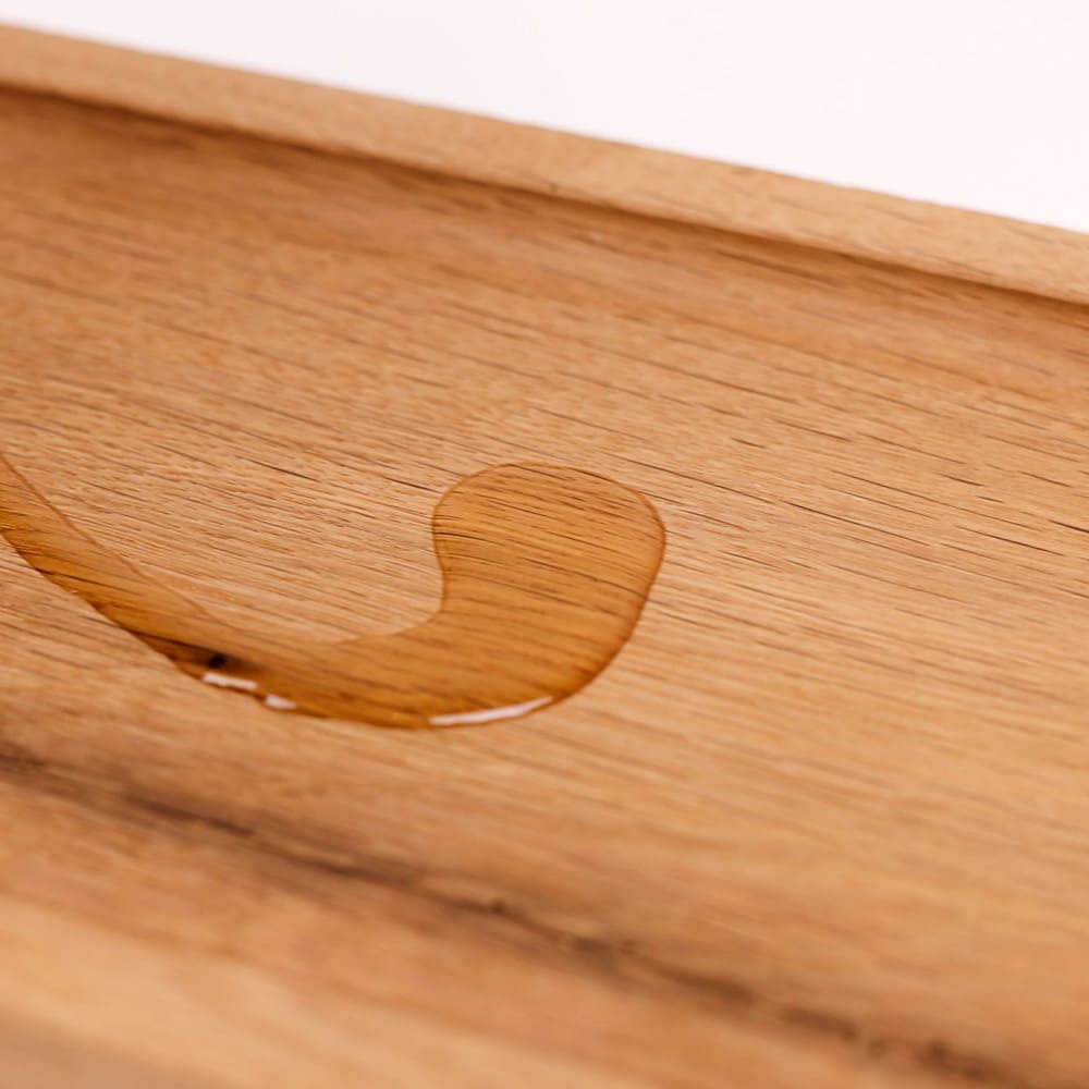 Holzpflegeöl in Lebensmittelqualität wurde auf ein Brett gegossen. Man sieht deutlich den Farbunterschied und die Holzmaserung tritt hervor.