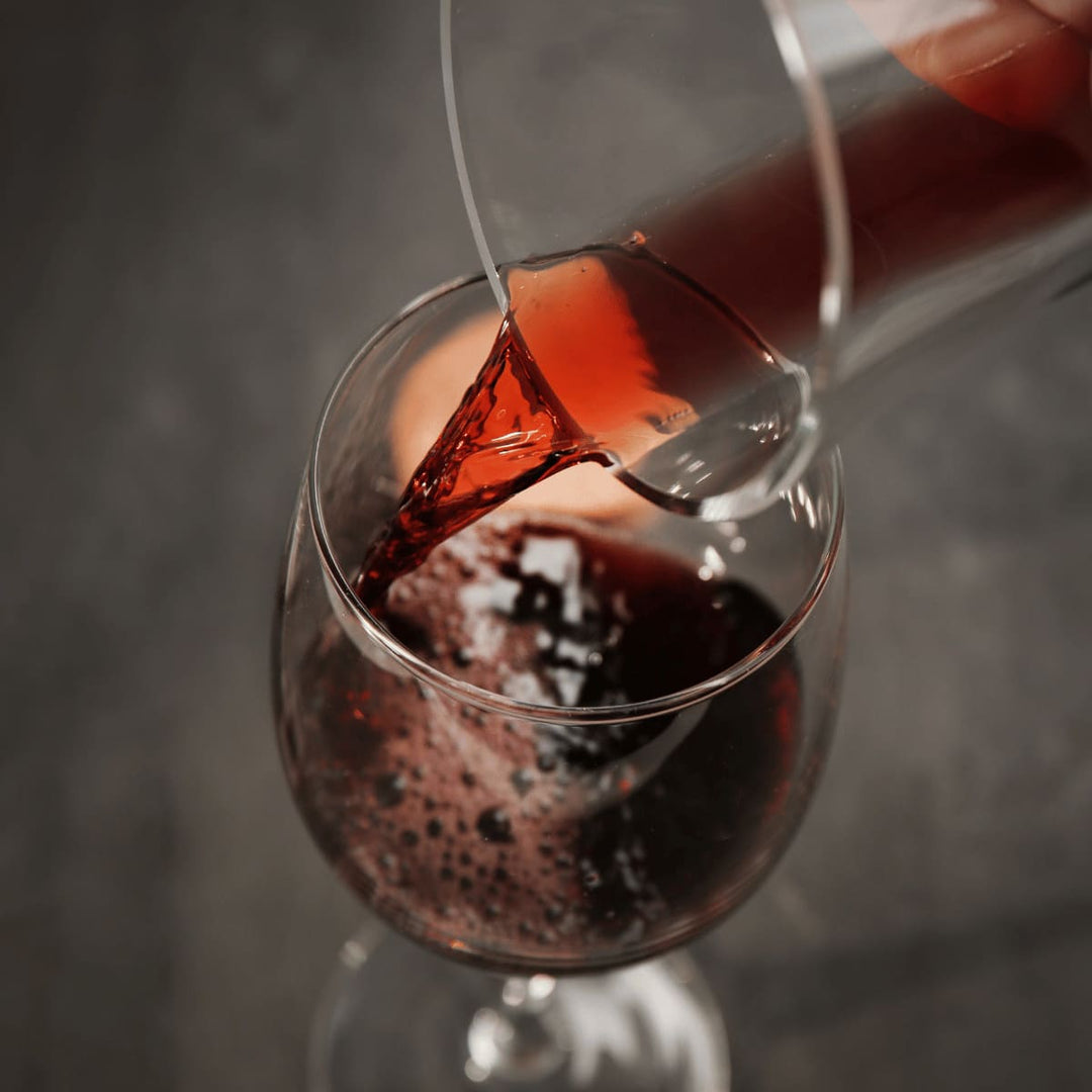 Aus einer zarten Glaskaraffe wird Rotwein in ein Weinglas gefüllt.