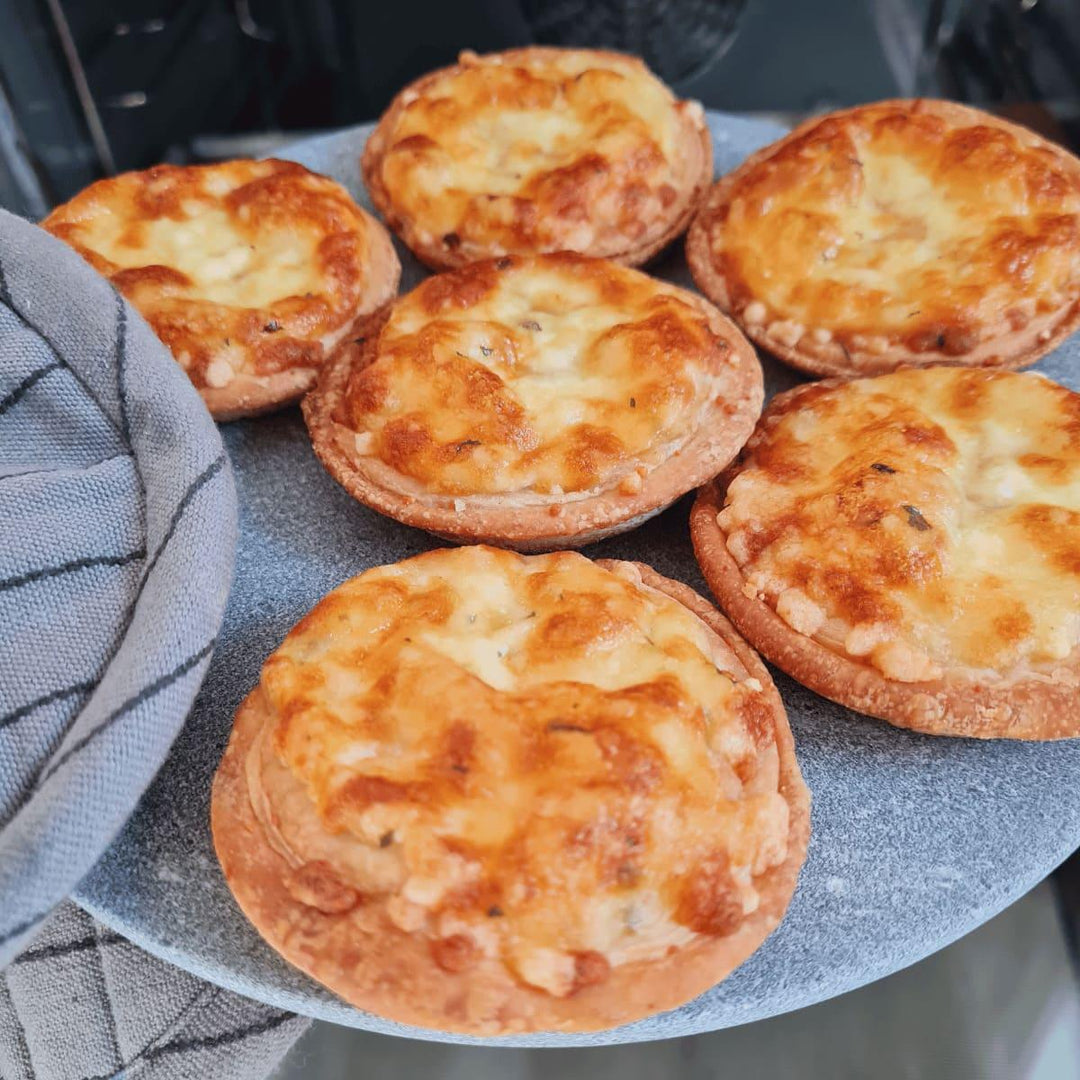 Einen grauen Teller aus Naturstein, karelischer Steatit aus Skandinavien, auf dem kleine Pizzen liegen. Eine Hand mit Topflappen holt den heißen Teller aus dem Ofen.