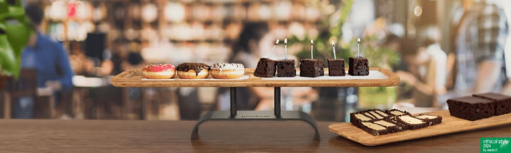 Etagere Hightray mit Platte von Juvahem, Mit Kuchen dekoriert im Hintergrund ist ein Café mit Menschen zu sehen