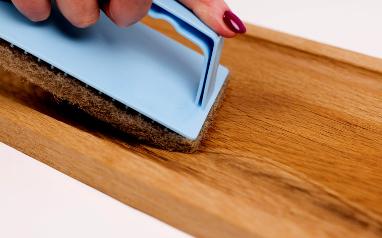 Nahaufnahme von einem Holztablett aus Eichen Altholz. Eine Hand ölt das Holz mit einem Ölpad in einem blauen Padhalter ein.