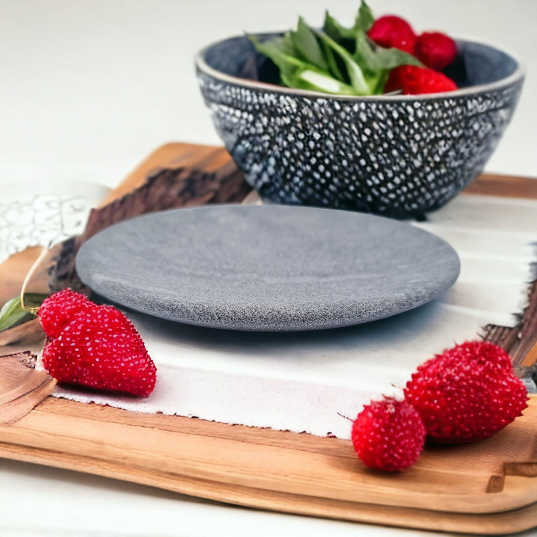 Steatit, ein Teller aus Naturstein steht auf einem Holzbrett, drumherum liegen rote Erdbeeren