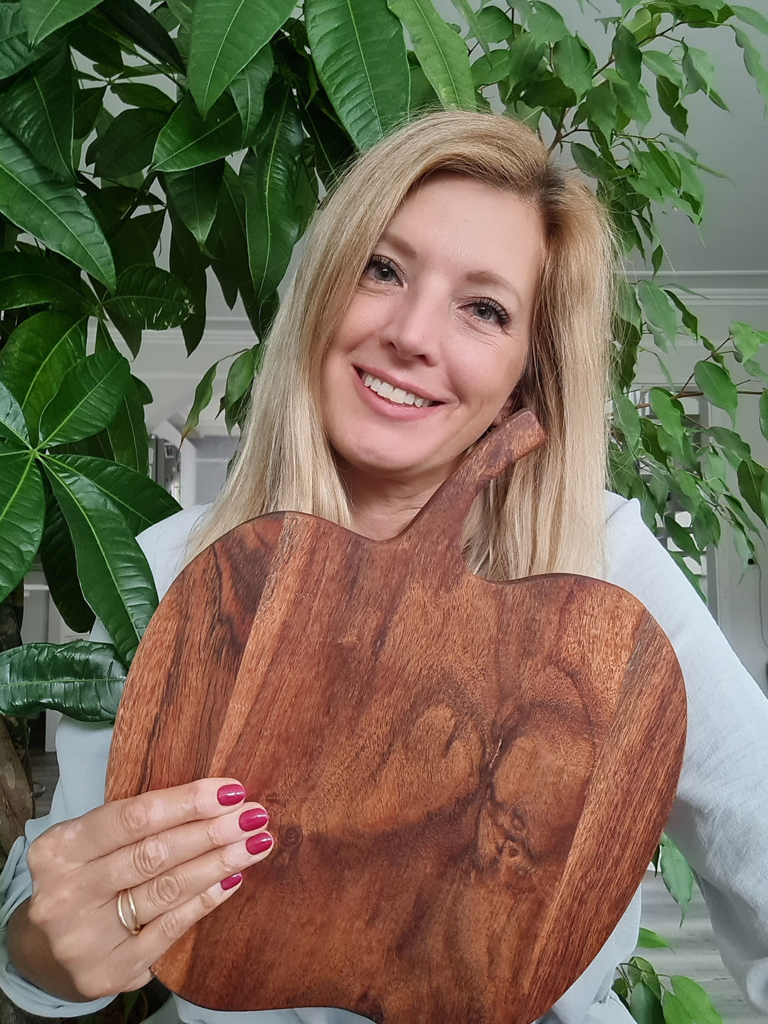 Eine blonde Frau hält ein Stück Holz unter einer Pflanze stehend und lächelt in die Kamera, Jil, die Gründerin der Firma Juvahem