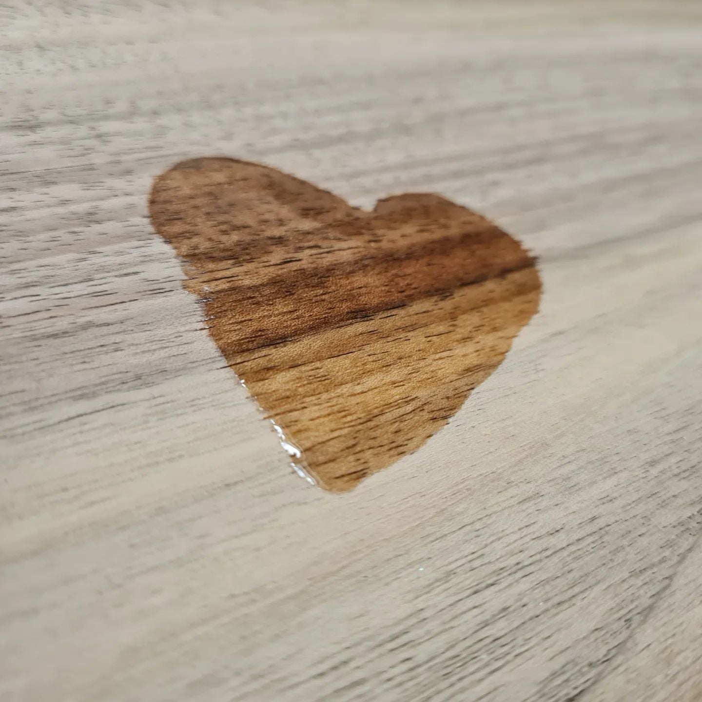 Mit Holzpflegeöl in Lebensmittelqualität wurde ein Herz auf ein Holzbrett gemalt. Man sieht deutlich den Farbunterschied und die Holzmaserung tritt hervor.