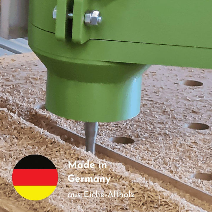 Ein Fräser fräst Altholz und es liegen Sägespäne auf der Arbeitsfläche. Eine deutsche Fahne erklärt, dass die Herstellung des Produkts in Deutschland stattfindet und es aus Eiche Altholz produziert wird.
