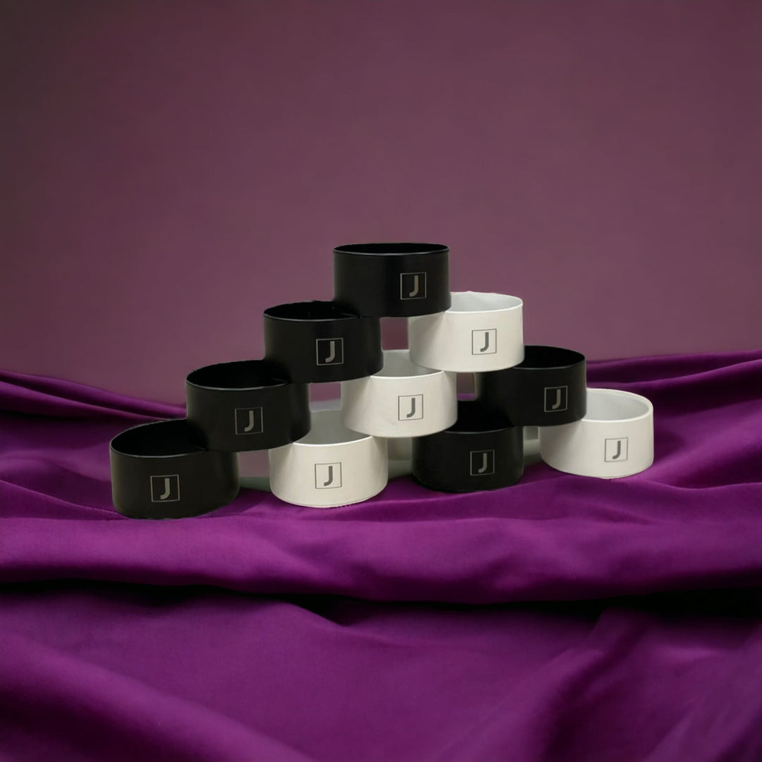 Metallringe in weiß und schwarz beschichtet mit dem Logo von Juvahem sind als Pyramide gestapelt auf einem violetten Seidentuch.