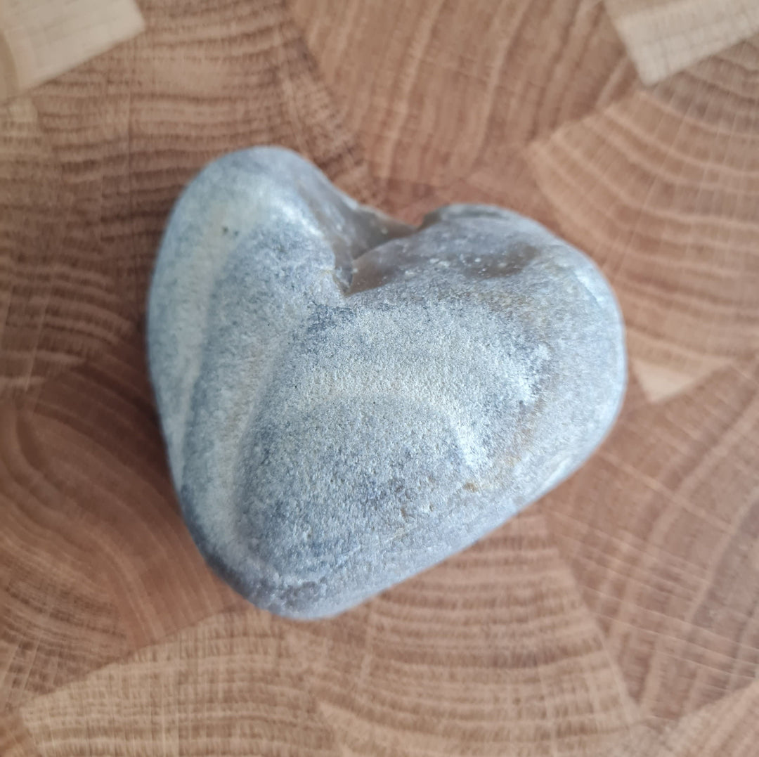 Ein Naturstein geformt wie ein Herz liegt auf einem Stirnholz Holzbrett. Der Stein soll dien Naturstein der Produkte von Juvahem signalisieren. Und die Liebe zur Nachhaltigkeit.