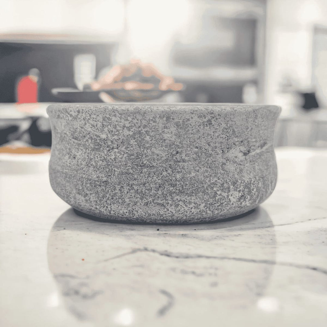 Eine große graue Schale aus Naturstein, karelischer Steatit aus Skandinavien, die man für Snacks, Lebensmittel, wie Obst nutzen kann, die in einer Küche auf der Marmor Arbeitsplatte steht.