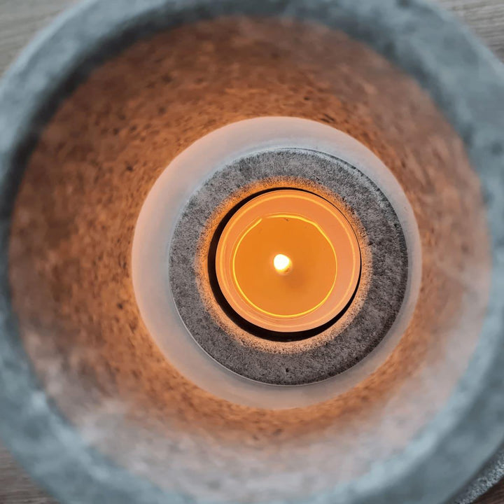 Sicht von oben in einen grauen Teelichthalter mit Milchglaseinsatz aus Naturstein, karelischer Steatit aus Skandinavien, den man mit handelsüblichen Teelichtern füllen kann. Die Kerze brennt.