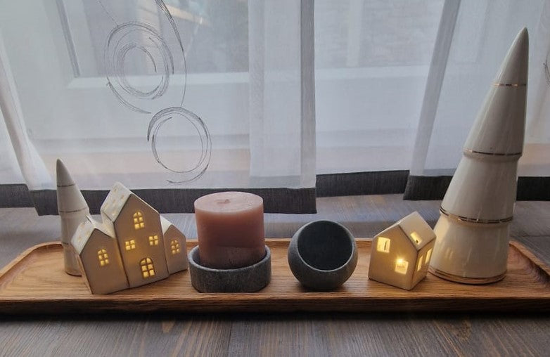 Das Holztablett Lowtray ist dekoriert mit einem Lichterhaus, Kerzen uns Natursteinschalen, es steht auf einem Holzboden vor einem Vorhang