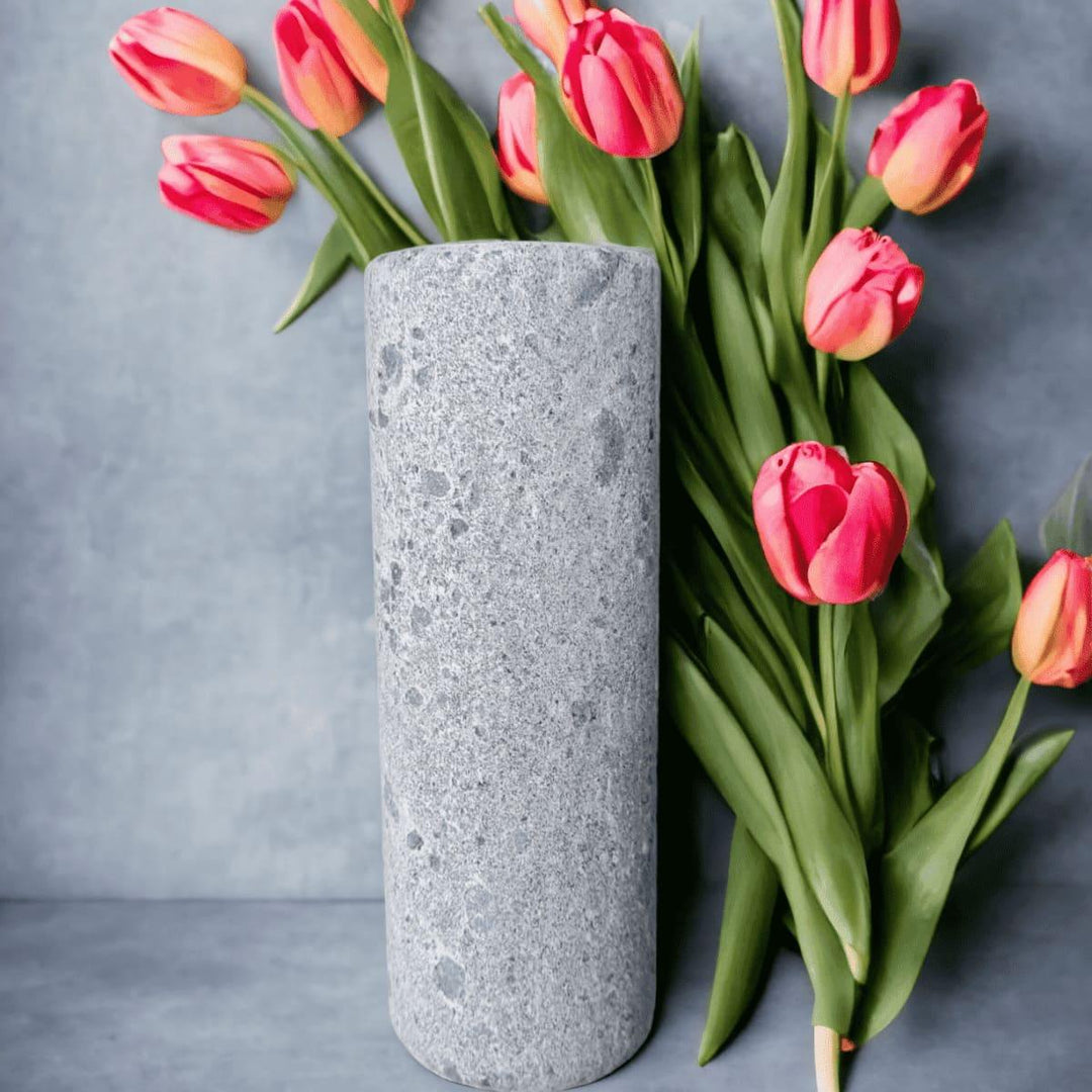 Eine graue, schmale Vase aus Naturstein, karelischer Steatit aus Skandinavien, die mit rosafarbenen Tulpen vor grauem Hintergrund dekoriert ist.