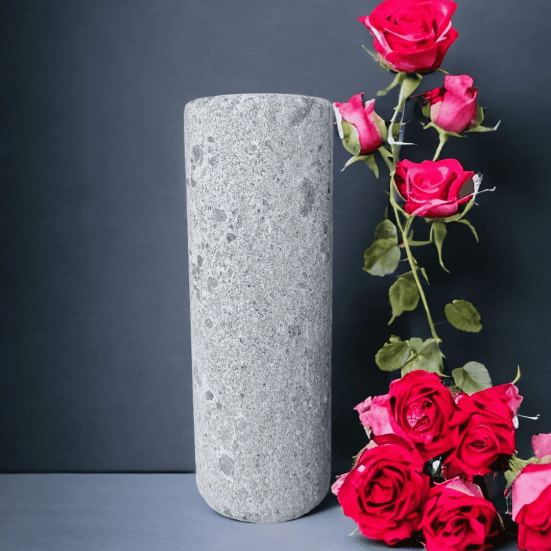 Eine graue, schmale Vase aus Naturstein, karelischer Steatit aus Skandinavien, die mit roten Rosen vor grauem Hintergrund dekoriert ist.