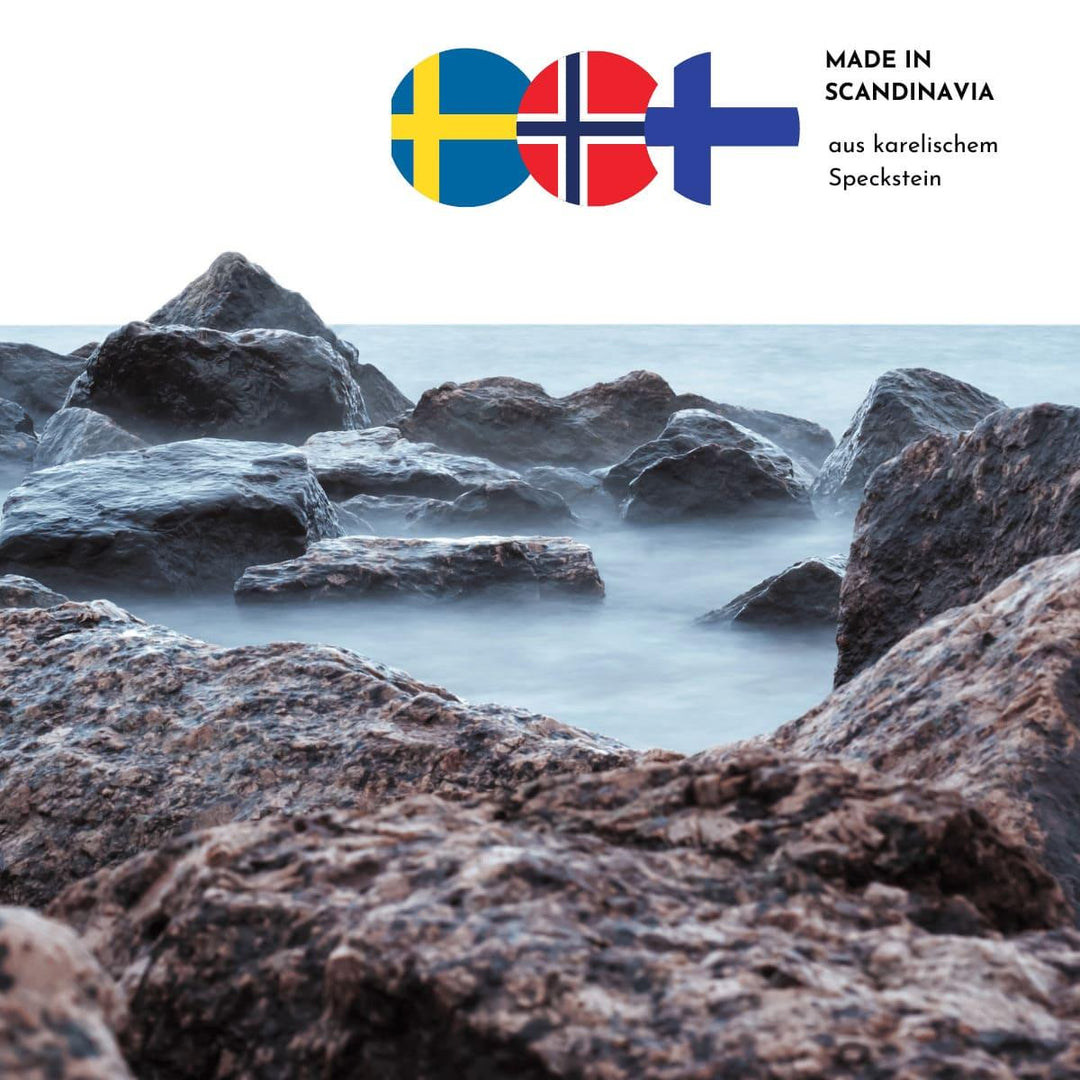 Raue Stimmung am Meer mit Felsformationen im unteren Bildrand. Drei skandinavische Flaggen und der Hinweis, dass die Produkte aus karelischem Speckstein sind, finden sich im oberen rechten Bildrand.