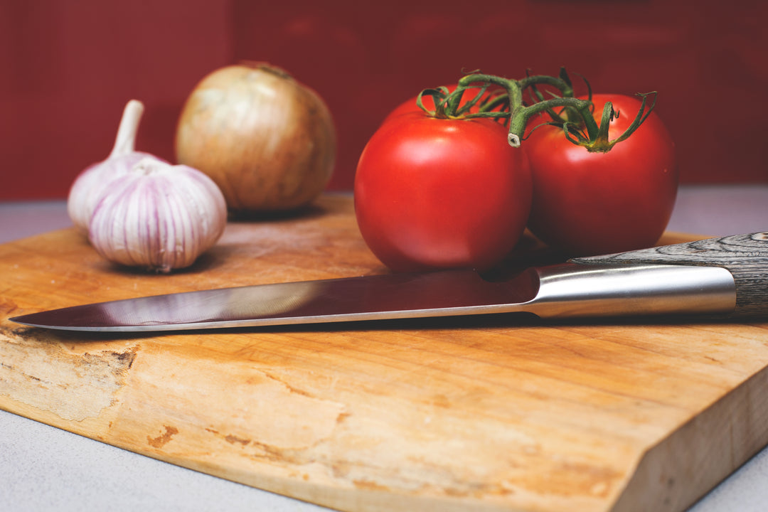 Tomaten, Zwiebeln und Knoblauch und ein hochwertiges Messer liegen auf einem Holzbrett von Juvahem